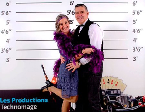 Couple élégamment habillé posant devant un décor rétro de casino et de voitures anciennes, photo prise lors d’un événement thématique festif.